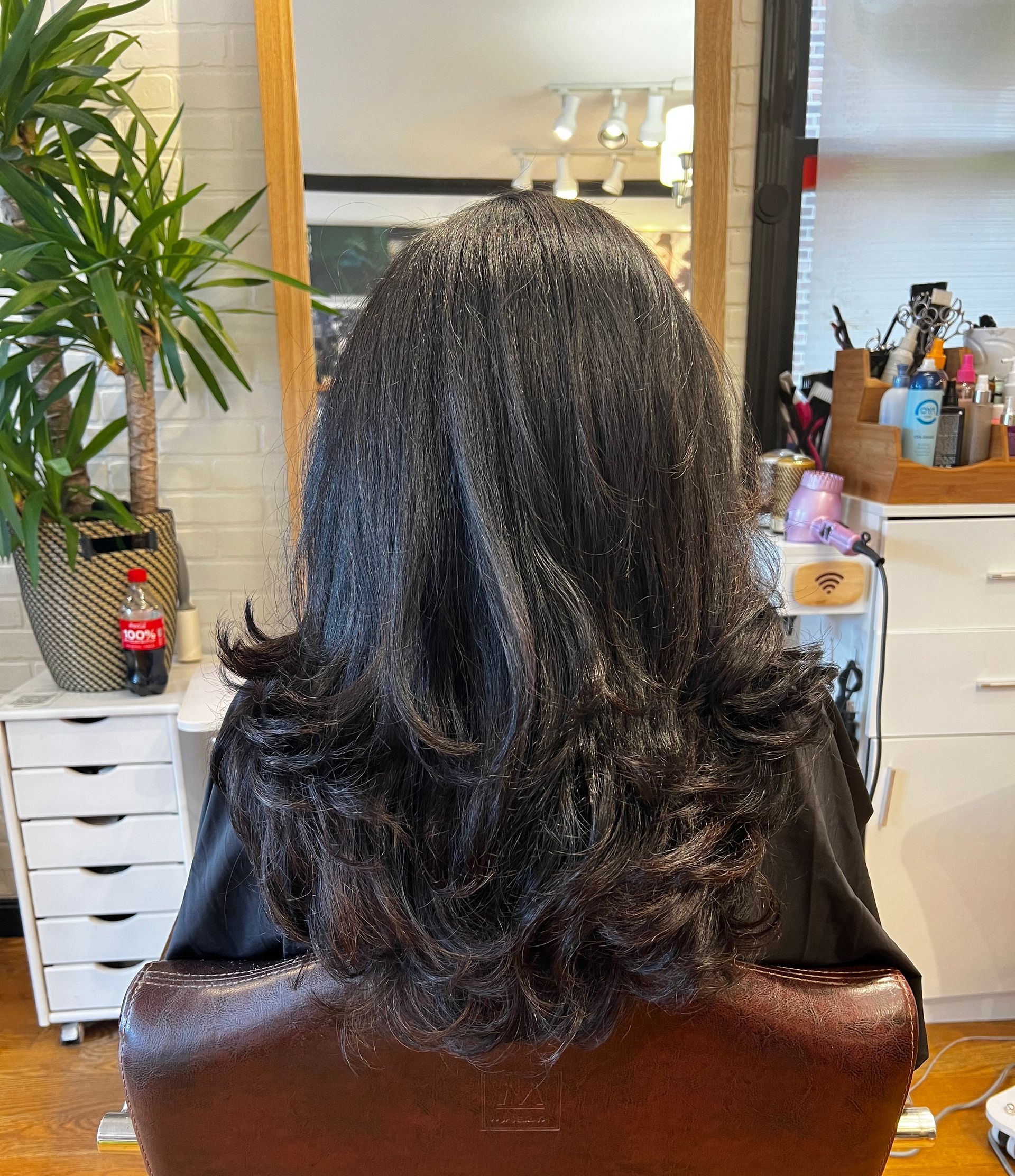 A woman with long hair is sitting in a chair in front of a mirror.