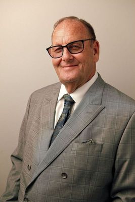 A man in a suit and tie is sitting at a desk with a name plate that says robert l. myers