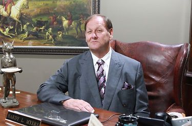 A man in a suit and tie is sitting at a desk with a name plate that says robert l. myers