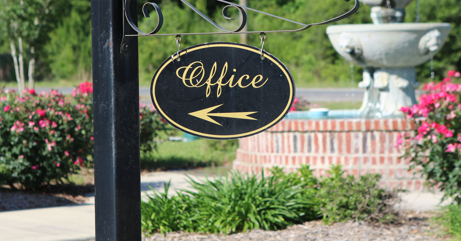 A sign for the office is hanging from a pole in front of a fountain.