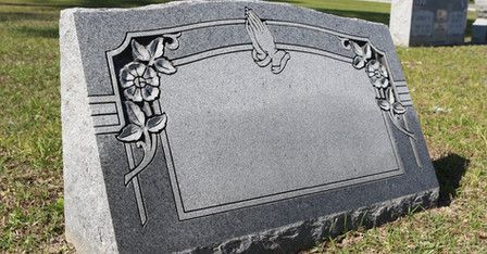 A gravestone is sitting in the grass in a cemetery.