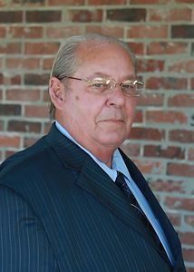 A man in a suit and tie is standing in front of a brick wall.