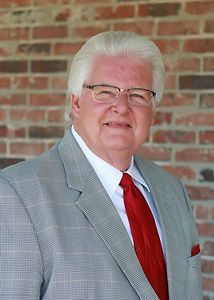 A man in a suit and tie is standing in front of a brick wall.
