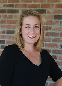 A woman in a black shirt is smiling in front of a brick wall.