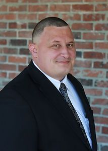 A man in a suit and tie is standing in front of a brick wall.