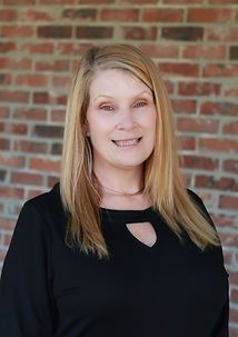 A woman in a black shirt is smiling in front of a brick wall.