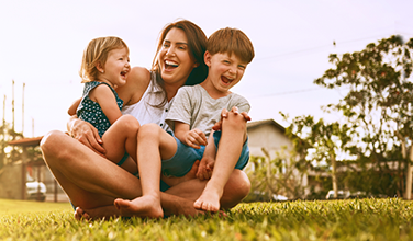 A woman is sitting on the grass with two children.