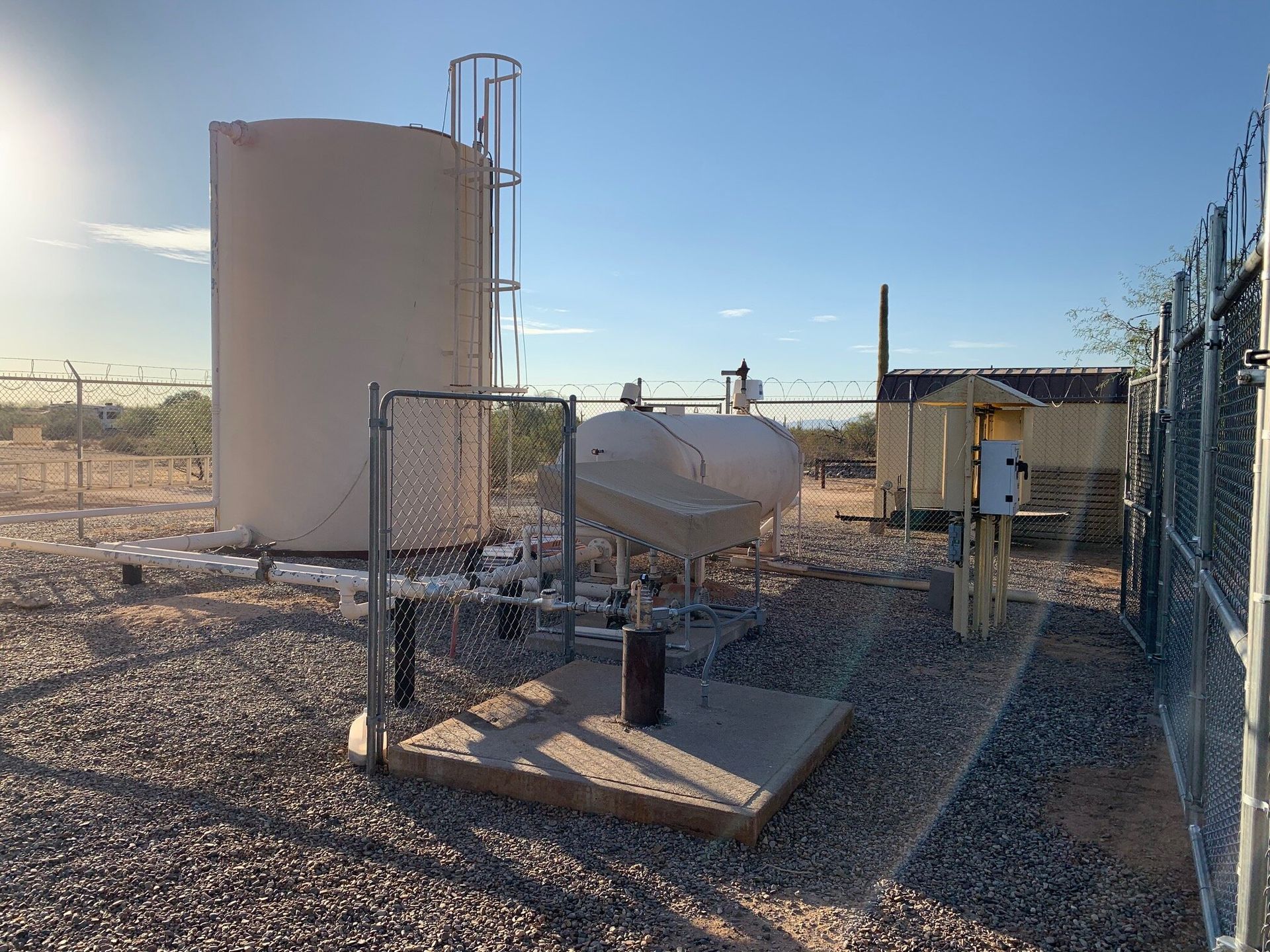 A large tank is sitting in the middle of a gravel field next to a fence.