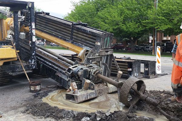 A man is standing next to a machine that is digging a hole in the ground.