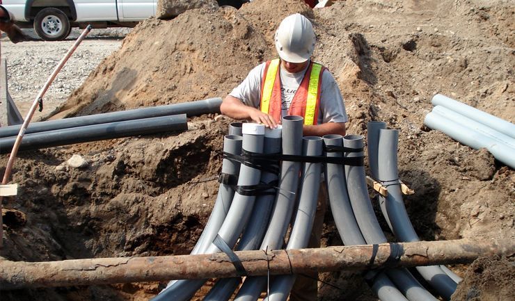A man is working on a bunch of pipes in the dirt
