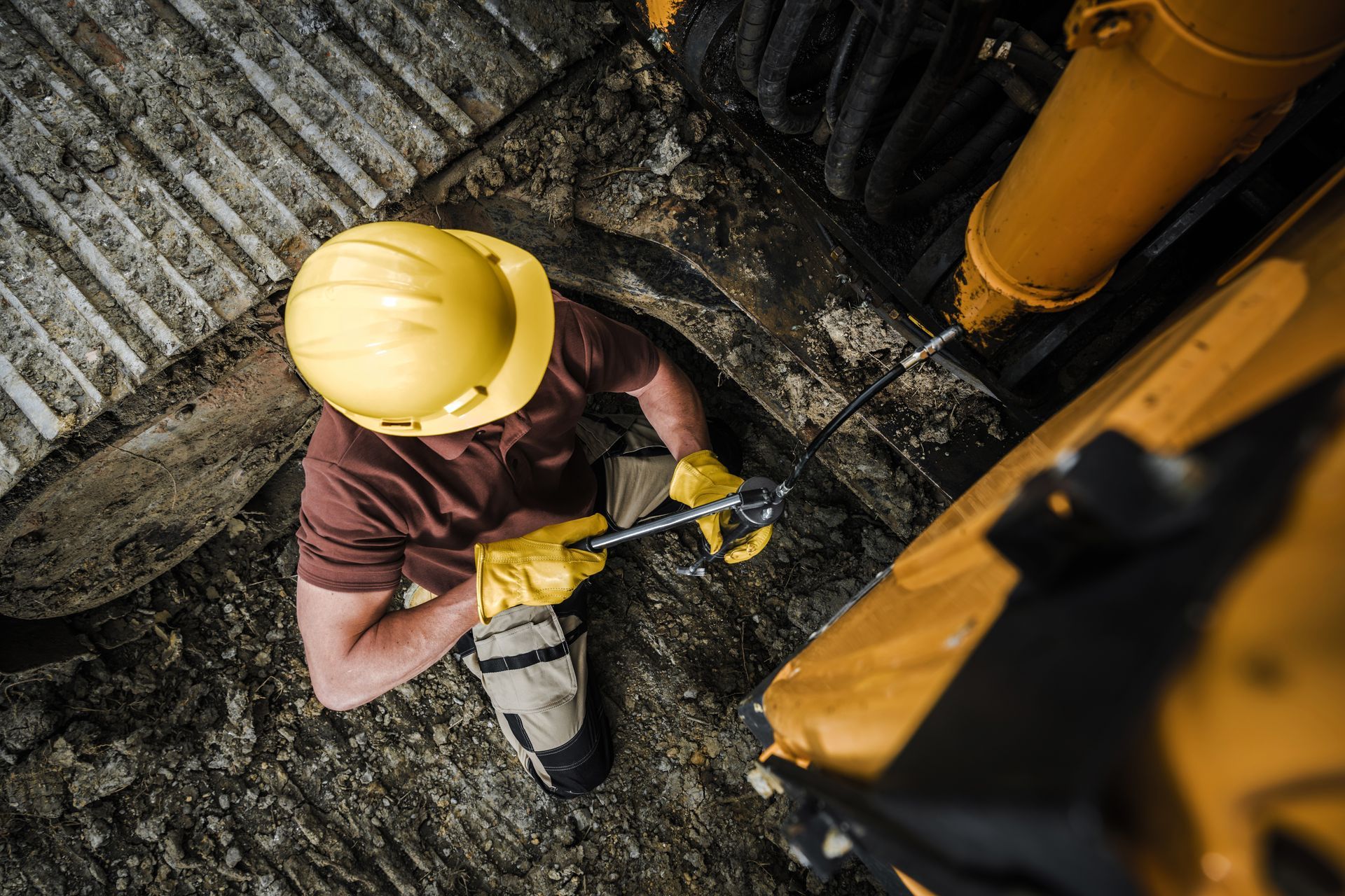 Person in a yellow hard hat and gloves working on a yellow construction machine.