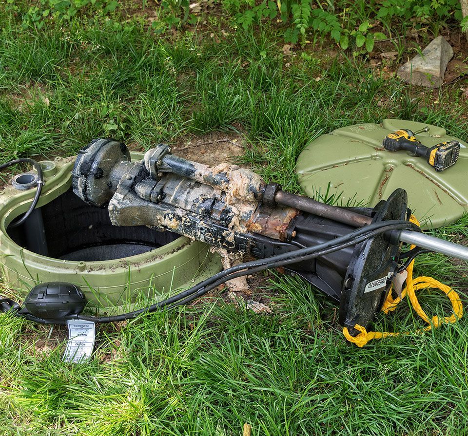 A broken machine is laying in the grass next to a drill.