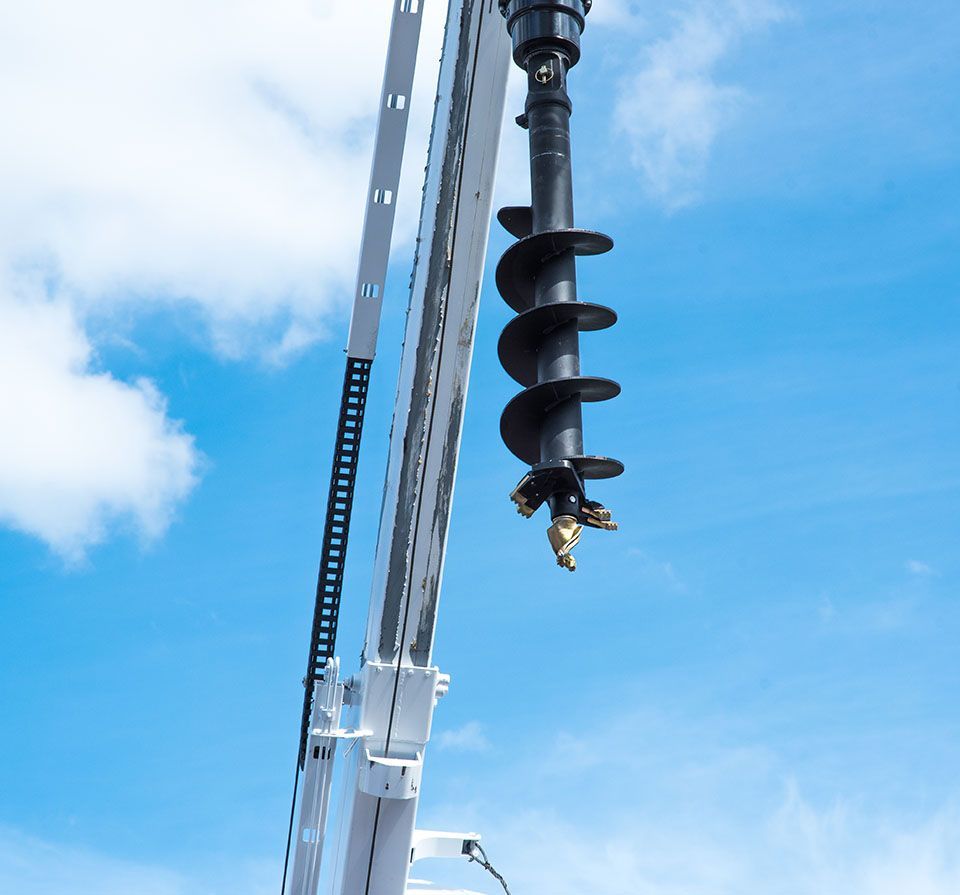 A drilling rig with a black auger against a blue sky with clouds.