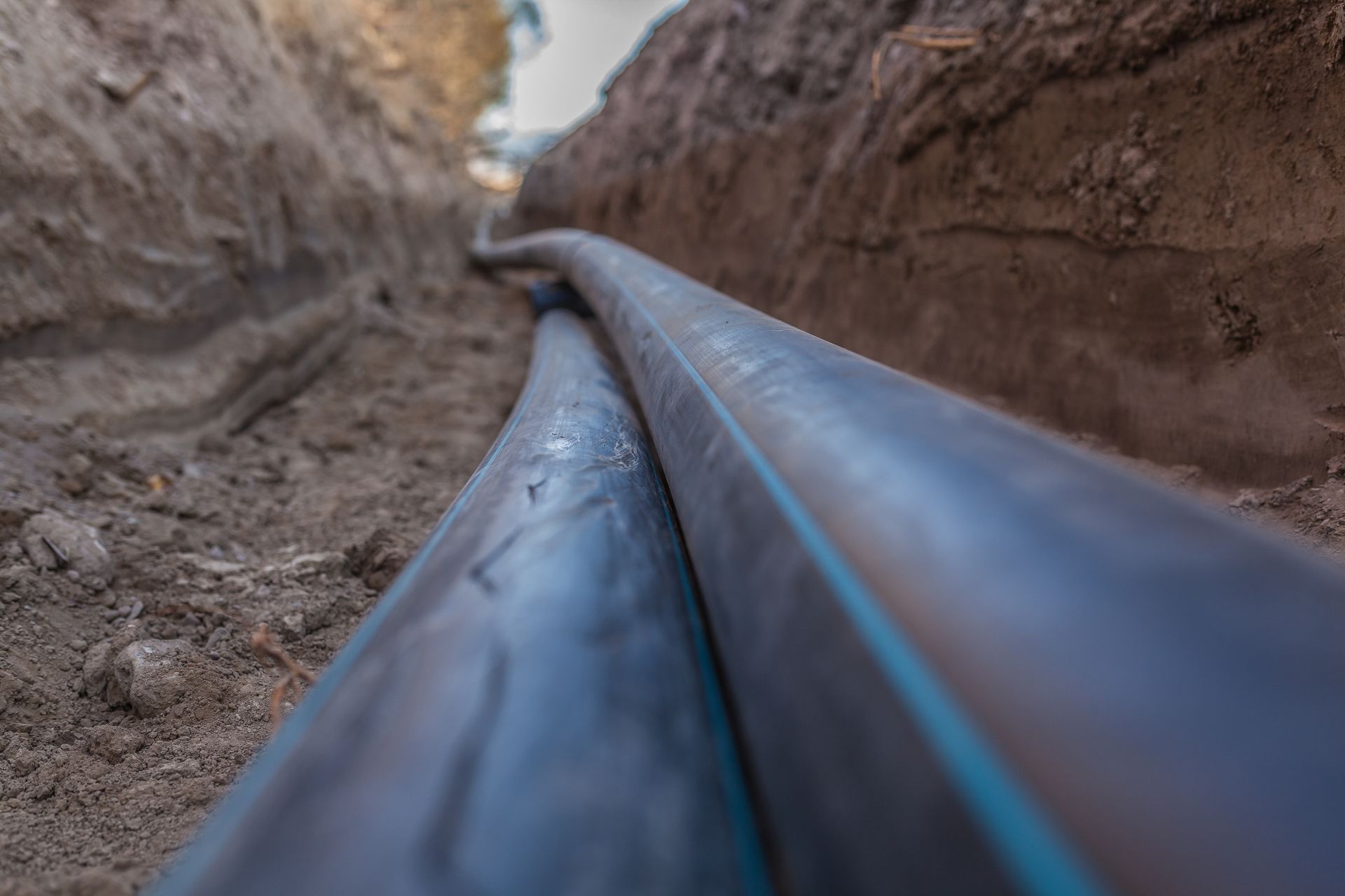 Two black pipes in a narrow trench, running parallel through dirt.