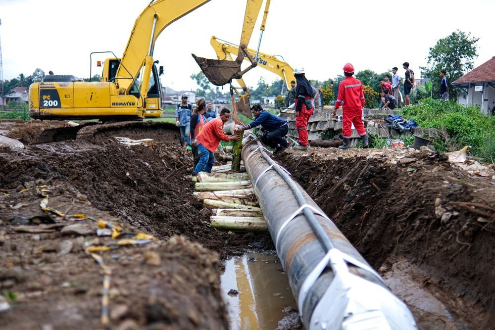 A group of construction workers are working on a pipe in the dirt.