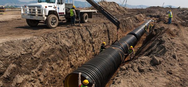 A group of construction workers are working on a large pipe in the dirt.