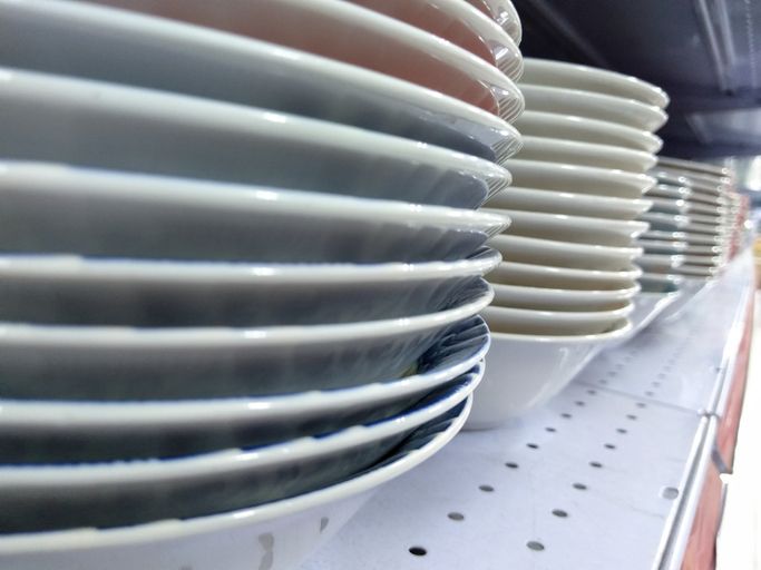 Pile di piatti bianchi, blu e beige su uno scaffale bianco in un negozio.