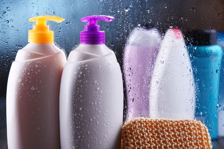 Flaconi di bagnoschiuma e shampoo su uno scaffale bagnato, con una spugna.