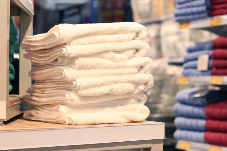 Pila di asciugamani bianchi sullo scaffale di un negozio, con scaffali sfocati di altri asciugamani colorati sullo sfondo.