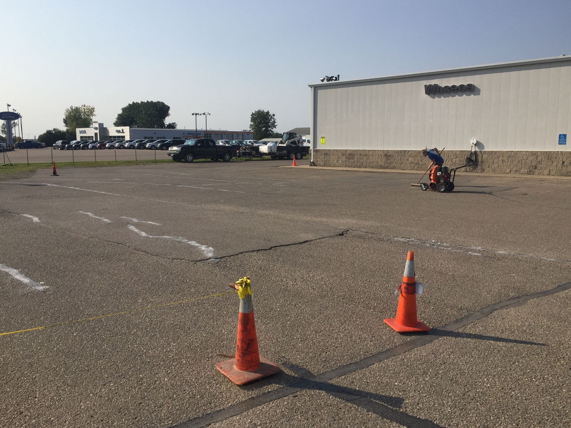 A person is riding a scooter in a parking lot with traffic cones.