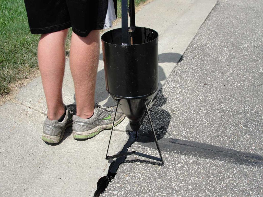 A person is standing next to a black bucket on a sidewalk.