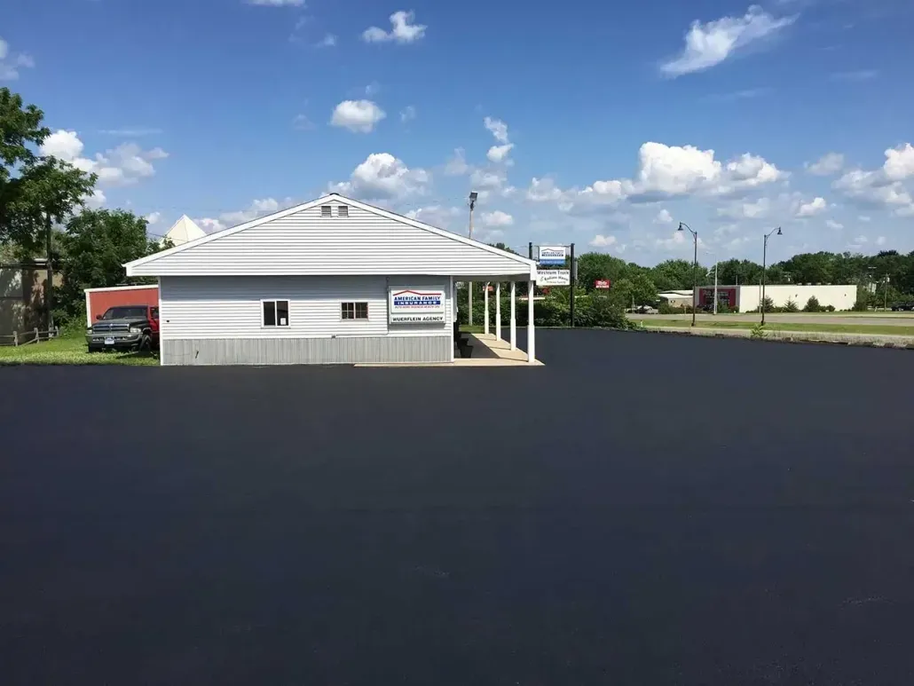 A white building is sitting on top of a black asphalt parking lot.