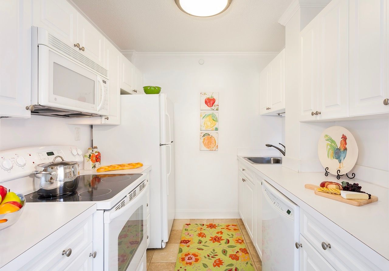 Bright white kitchen in an apartment with white cabinets, refrigerator, stove, microwave, and sink.