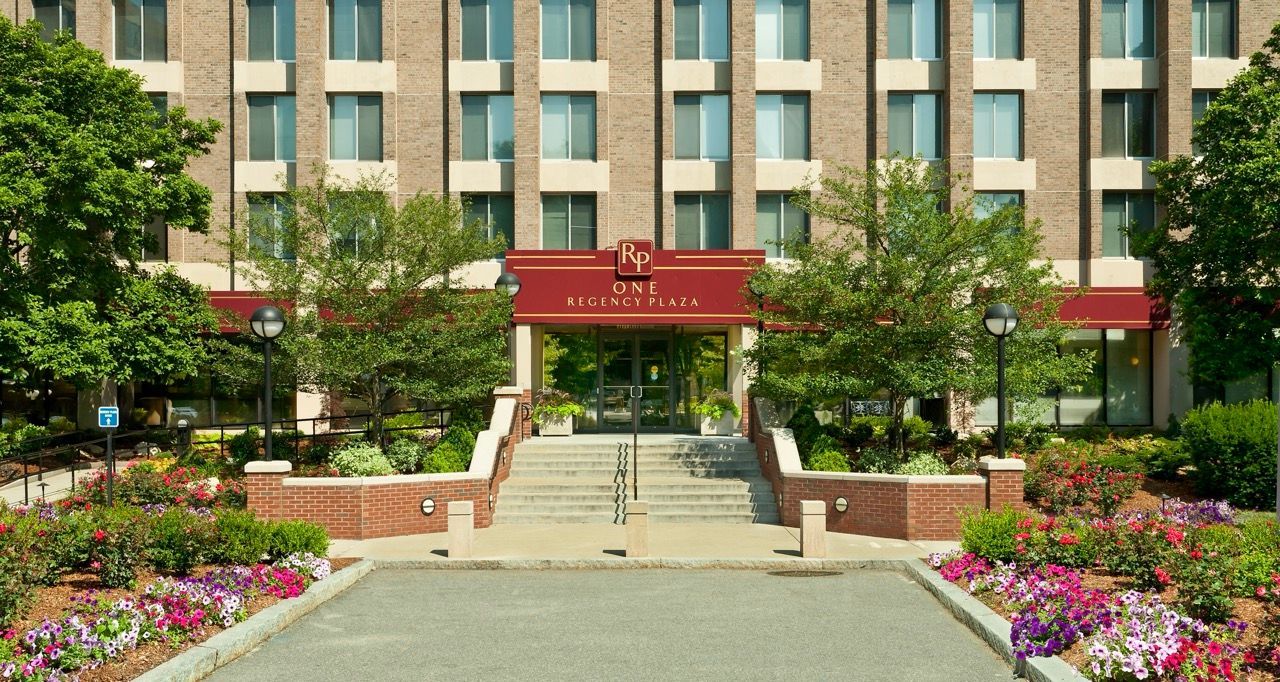 Entrance to a mid-rise apartment building with steps, a ramp, and landscaped entry plaza.