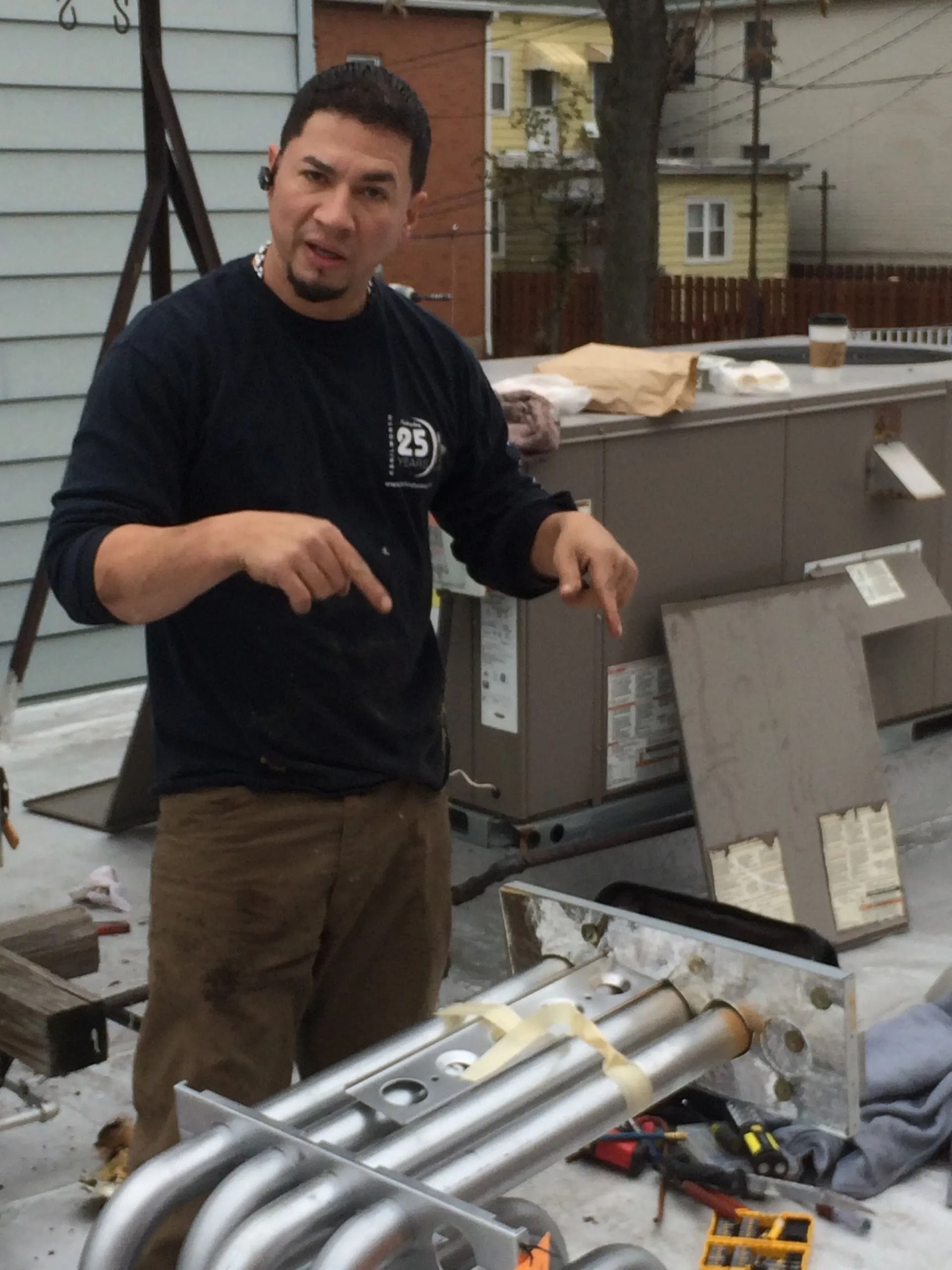 Man in work clothes points at HVAC parts on a rooftop.