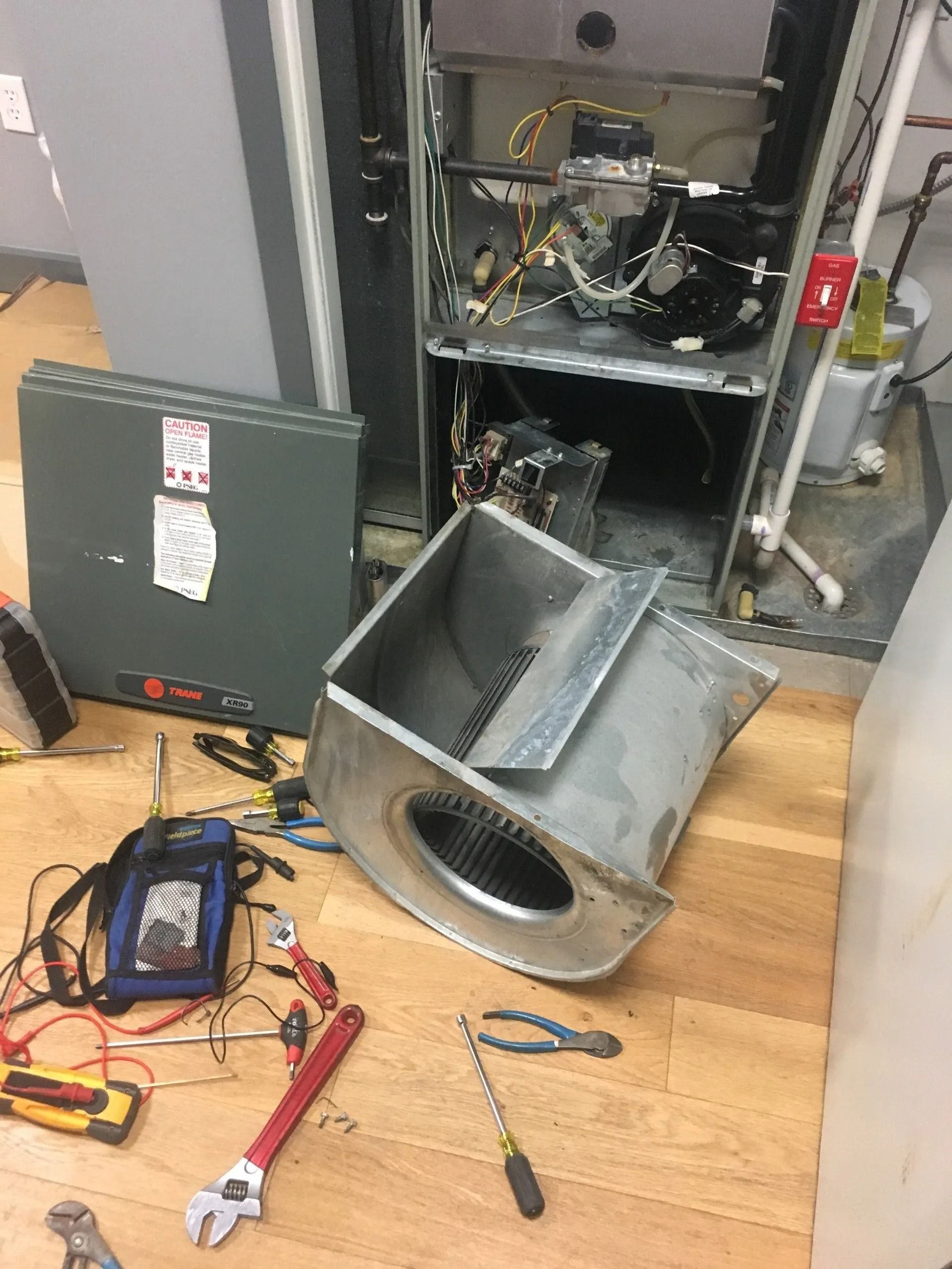 Furnace being repaired; open cabinet, blower fan detached, tools scattered on floor.