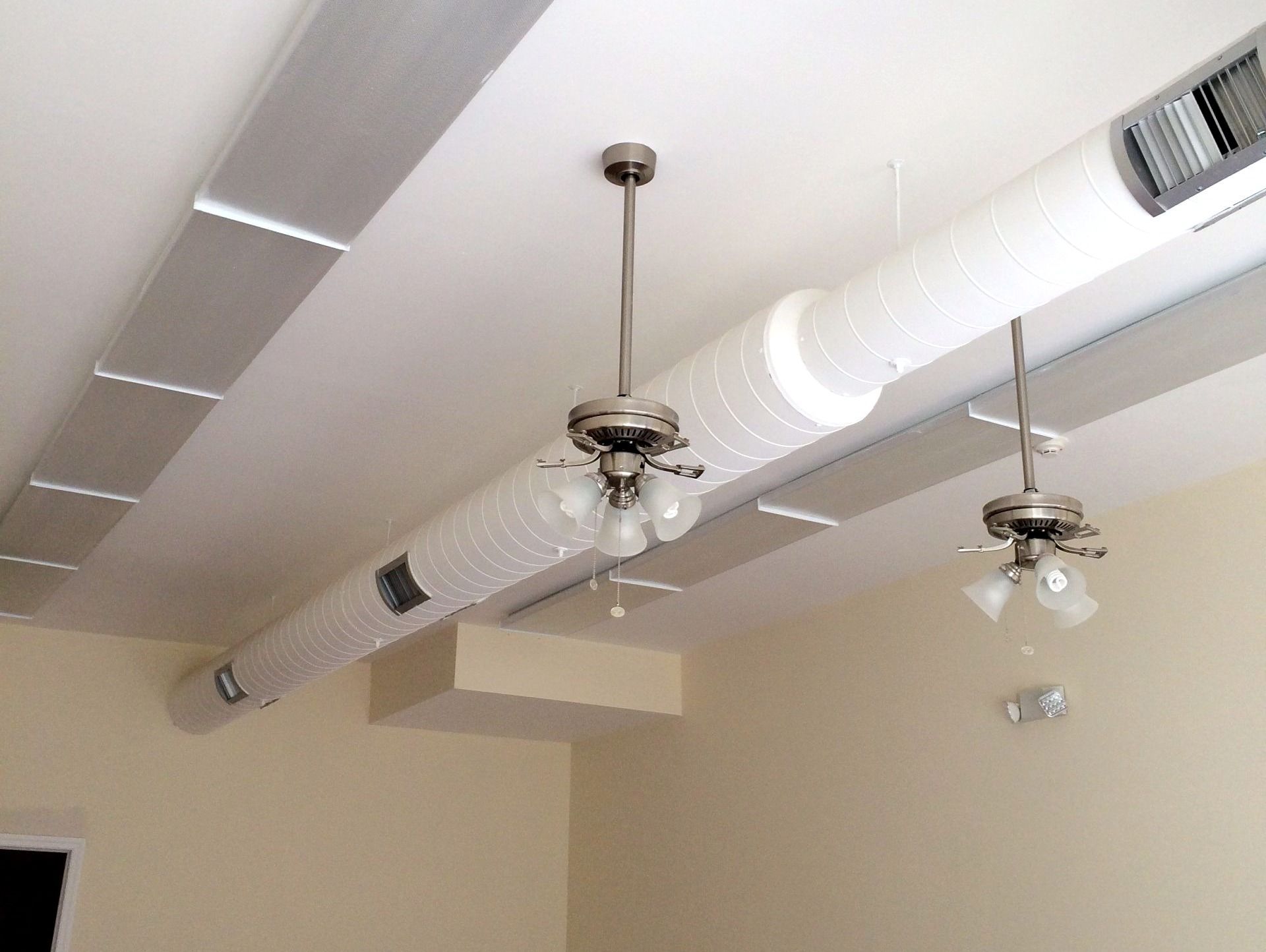 Two ceiling fans and ductwork on a white ceiling, with cream-colored walls.
