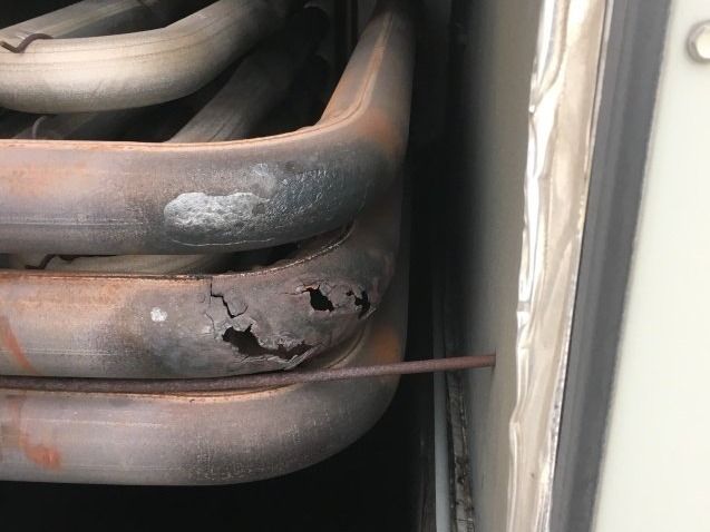 Corroded metal tubes with holes, likely from a furnace. Black soot and rust present.