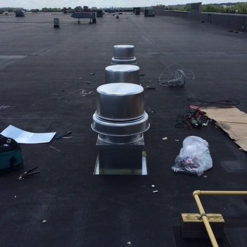 Row of rooftop exhaust vents on a black tar surface; work in progress.