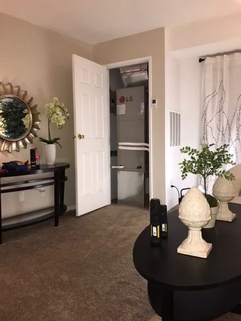 Living room with open closet containing HVAC unit. Dark table with decorations, mirror, and curtains.