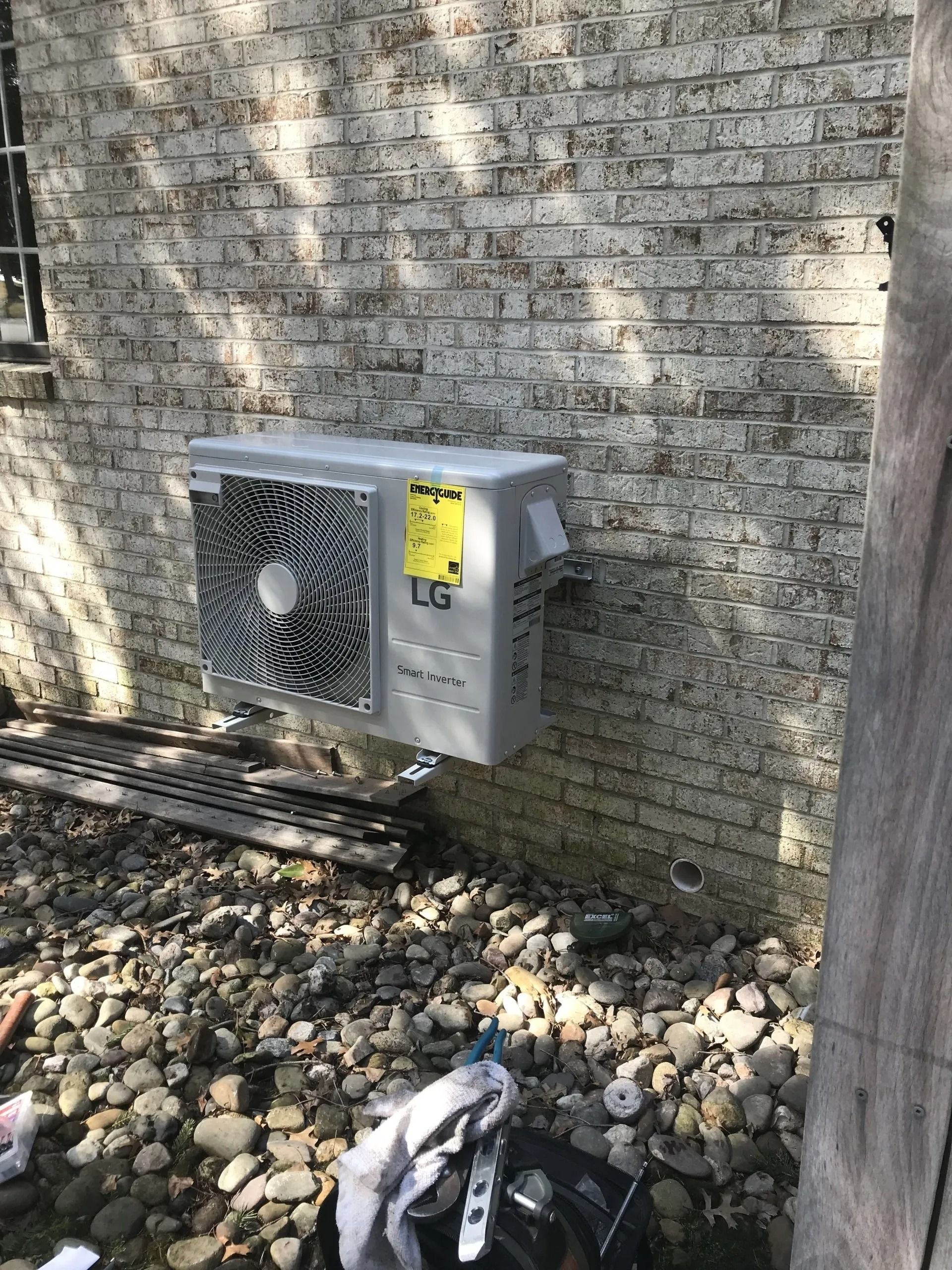 LG air conditioner mounted on a weathered brick wall; debris and rocks below.