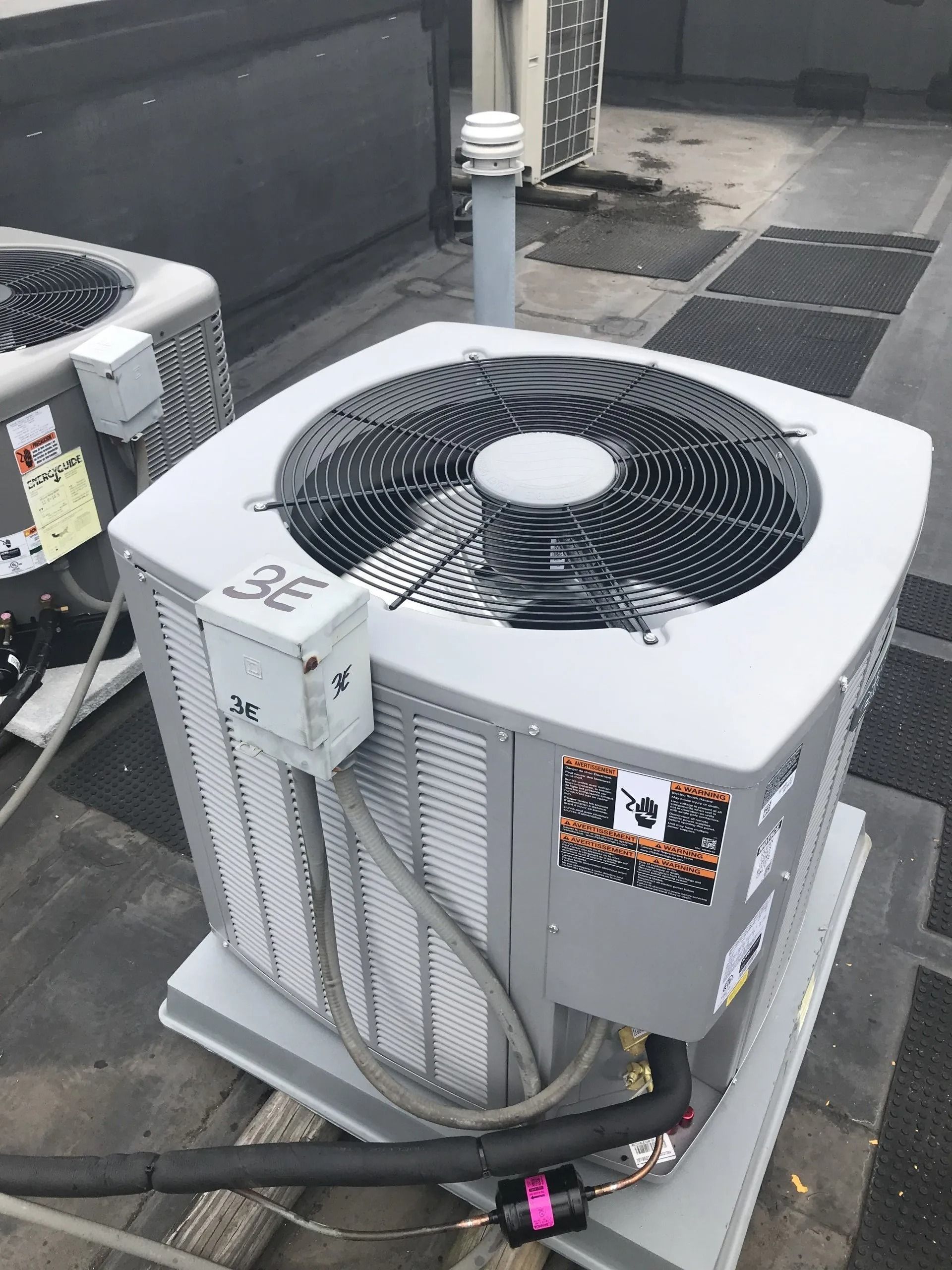 Gray air conditioning unit on a rooftop with a fan and visible wiring.