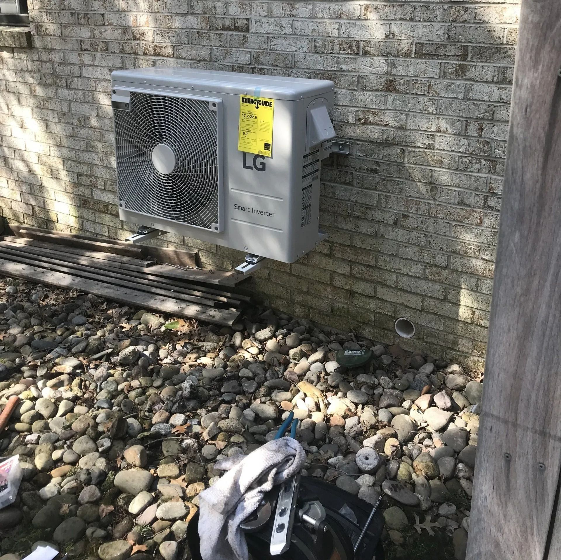 LG outdoor heat pump mounted on a brick wall above gravel.