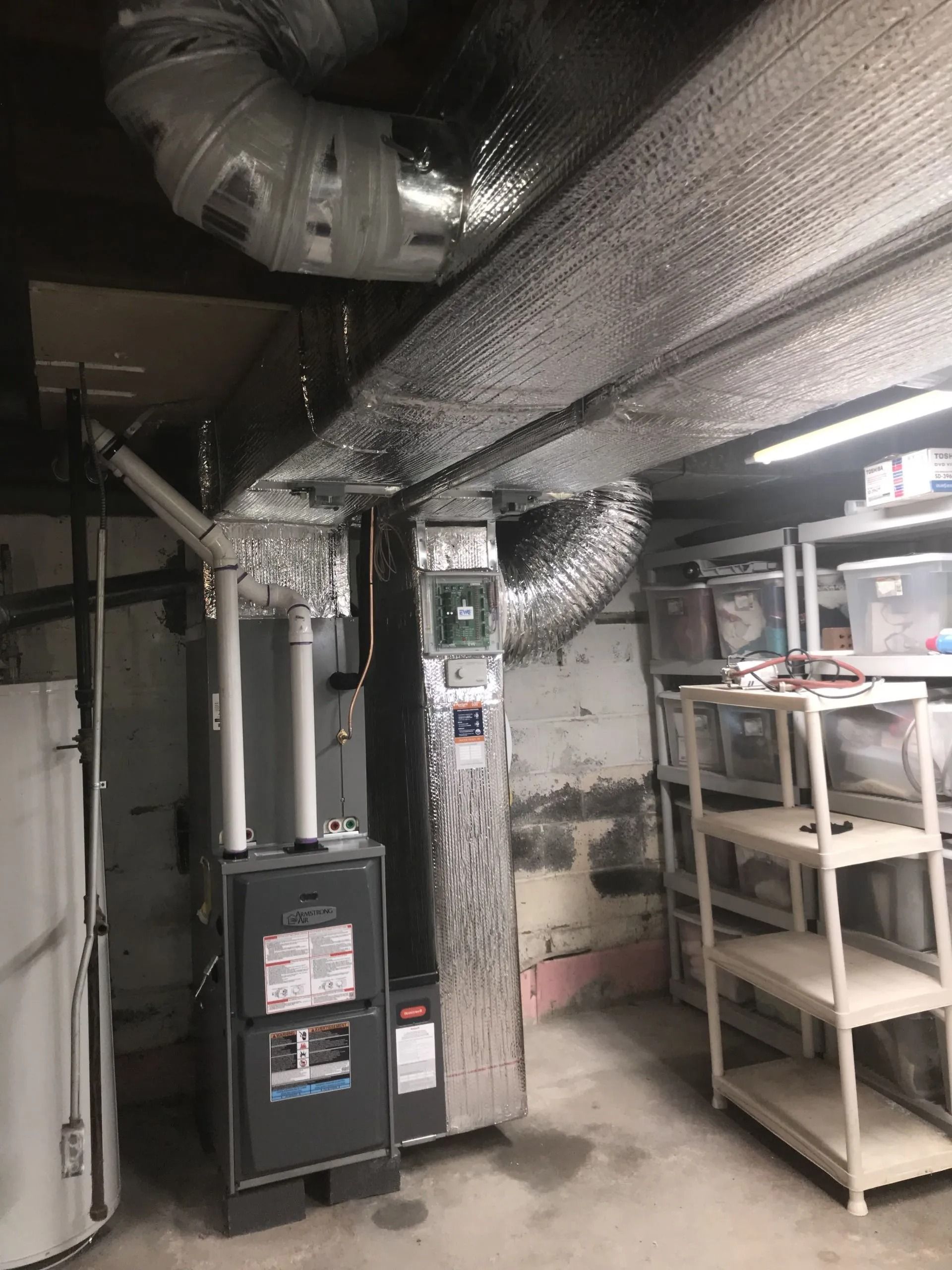 Furnace and ductwork in a basement, surrounded by shelves and storage.