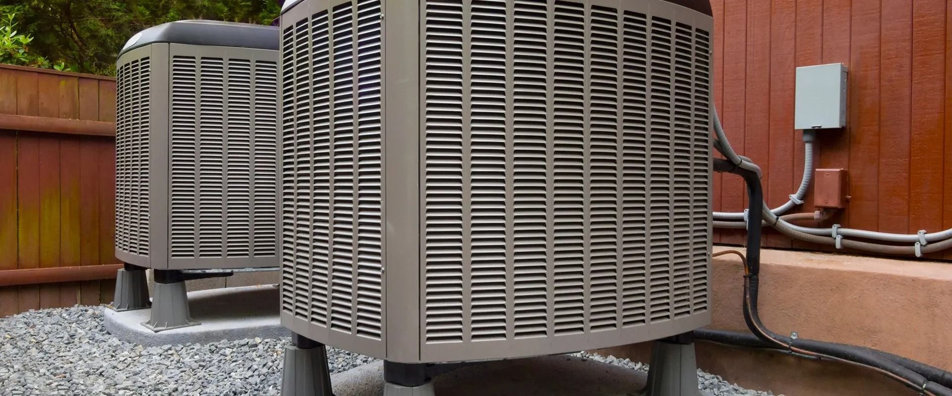 Air conditioning units on concrete pads next to a wooden structure.