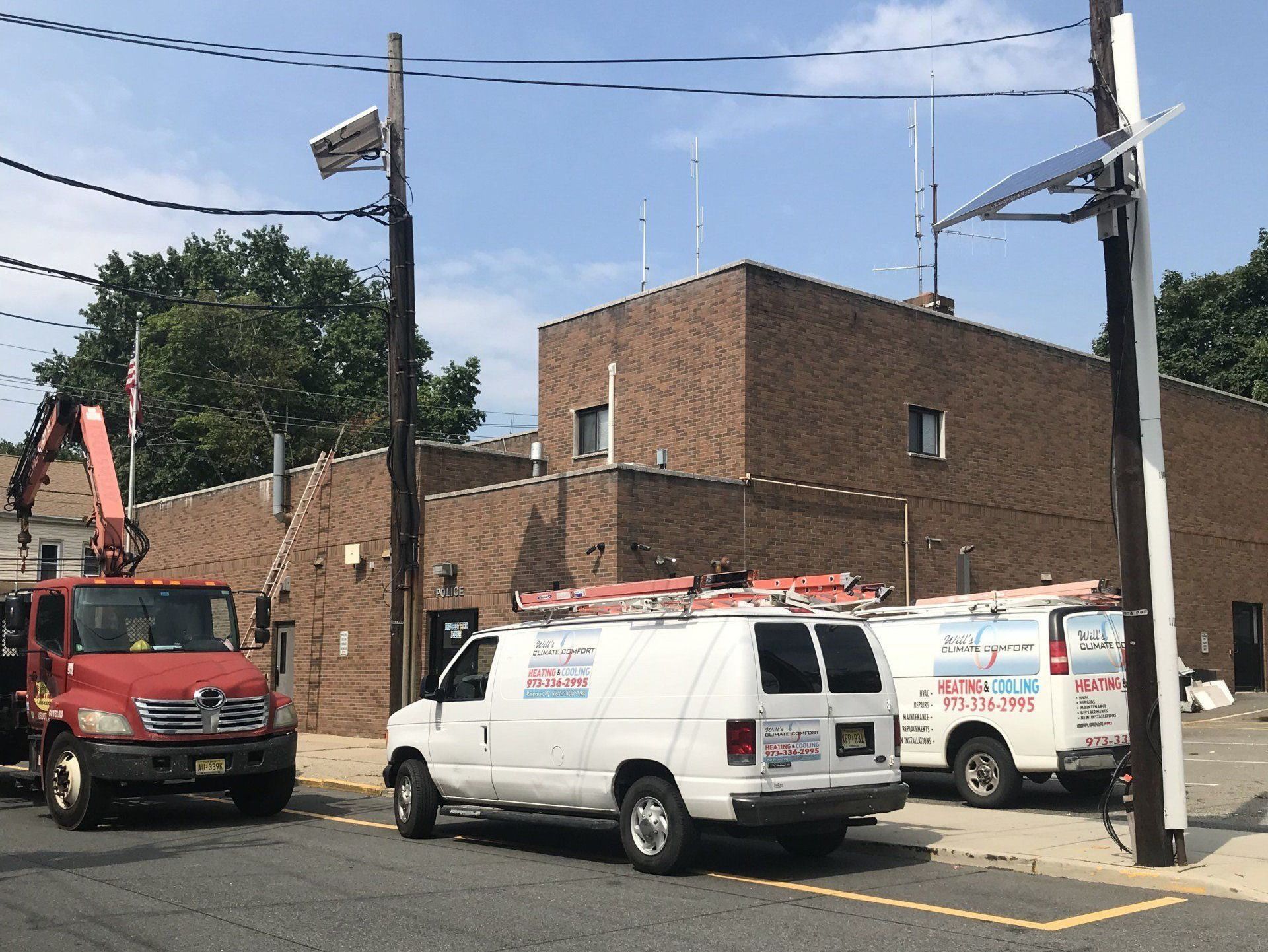 Red truck and white vans parked in front of a brick building on a sunny day.