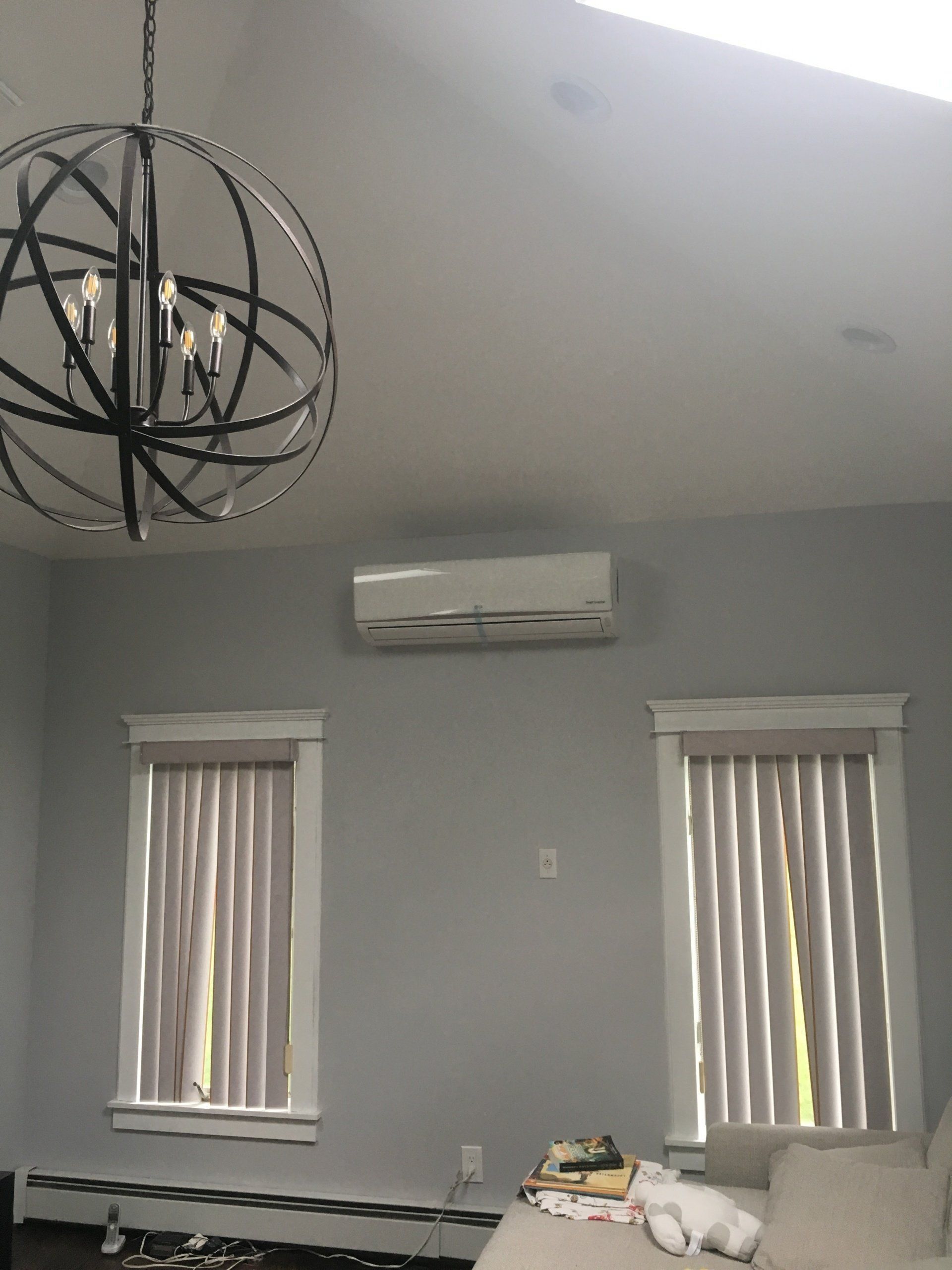 A light gray room with a chandelier, AC unit, two windows with blinds, and a couch.