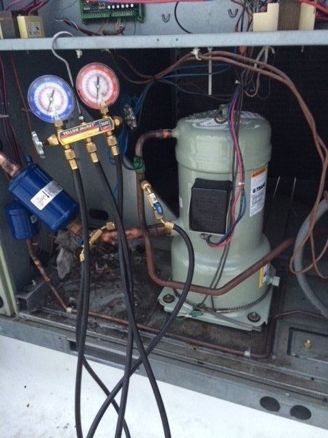 HVAC unit interior with gauges, refrigerant hoses, compressor, and blue filter drier.