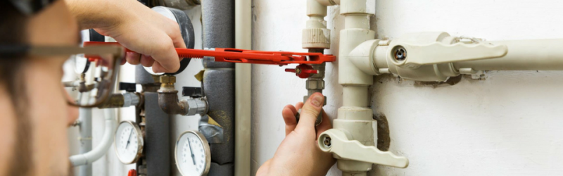 A person using a wrench to work on pipes near gauges and valves.