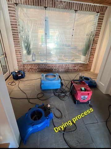 Water damage drying process inside a room, with plastic sheeting and multiple dehumidifiers.