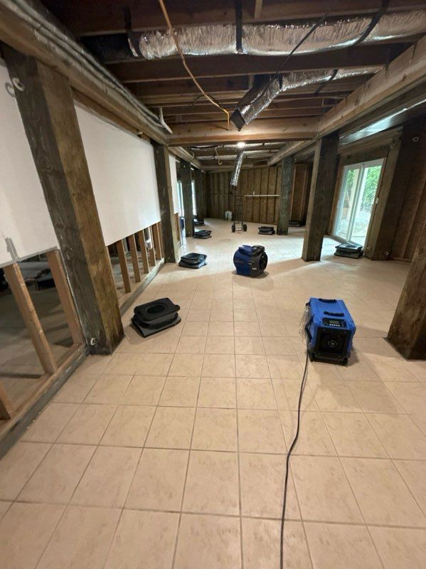 Basement with exposed beams, tiled floor, and several blue and black dehumidifiers.