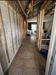 A hallway under renovation, with exposed framing, cinder block walls, and tile flooring.