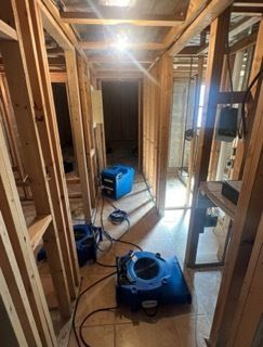 Hallway under construction with three blue air movers; bare wooden framing and tile floor.