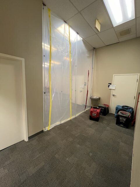Office hallway with a plastic barrier taped to the walls. Generators and equipment sit outside the barrier.