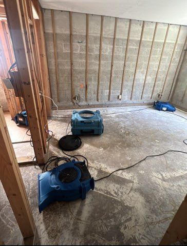 A room undergoing water damage restoration, with several blue fans and exposed wall studs.