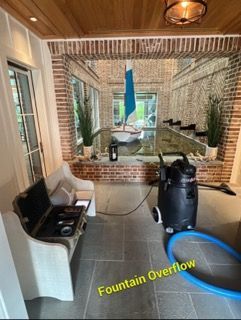 Indoor space with a brick wall and a water feature overflowing, near a sofa and vacuum.